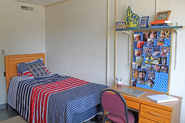 Inside of a single occupancy room inside Merici Hall. There is a bed, desk, and shelf.